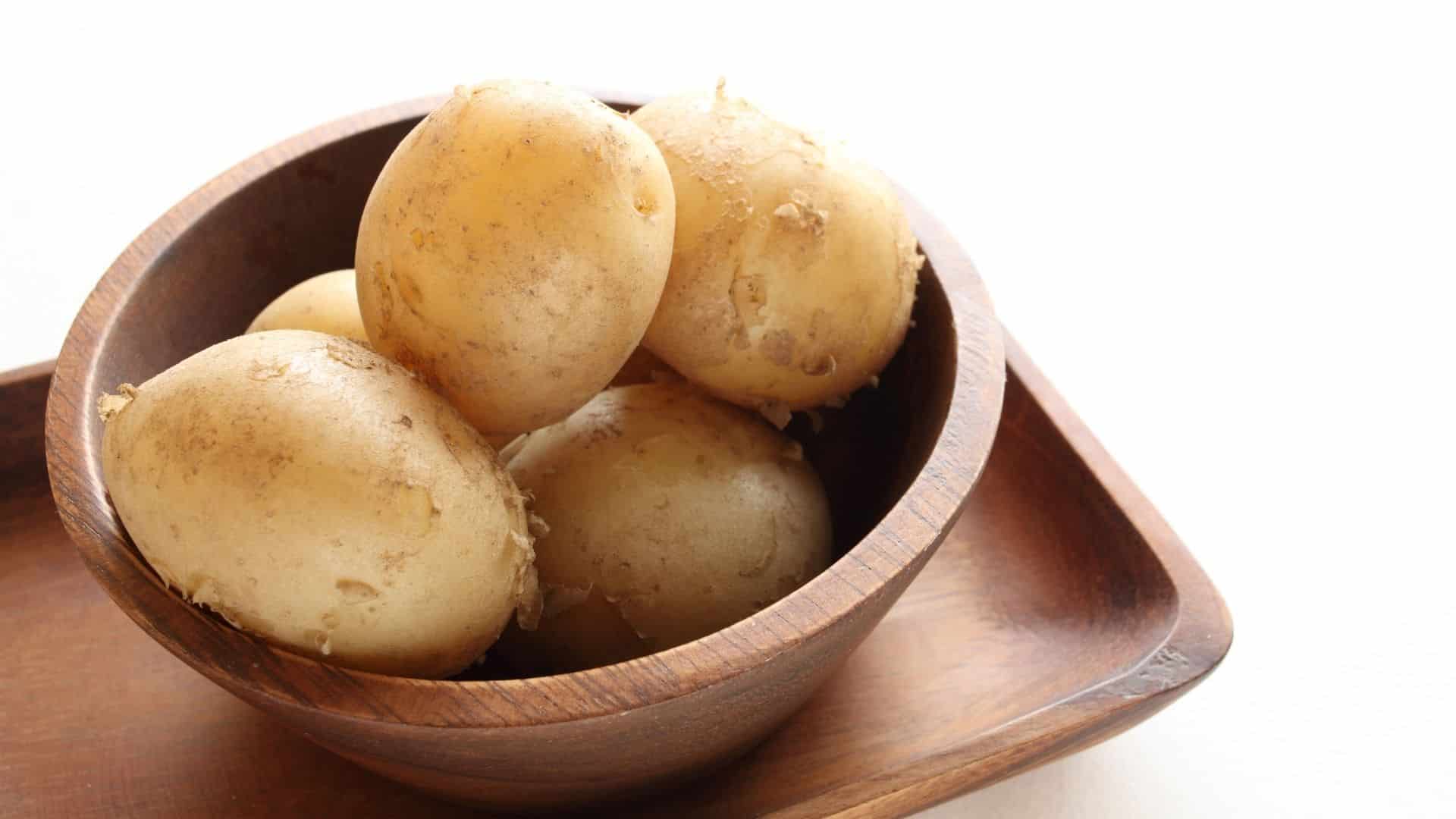 Eine Holzschale mit gekochten Kartoffeln steht auf einem Tisch.