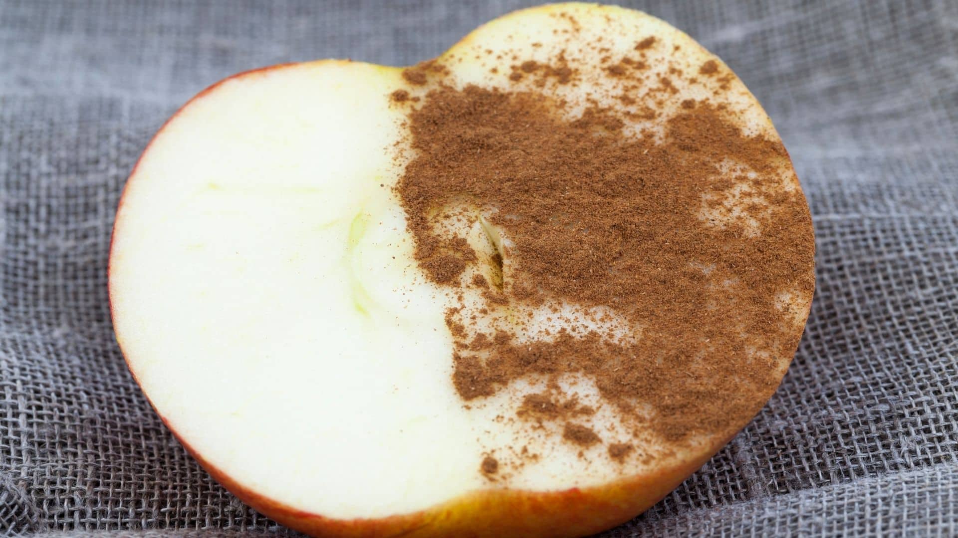 Ein halb aufgeschnittener Apfel liegt auf einem Handtuch. Er ist zur Hälfte mit Zimt bestreut.