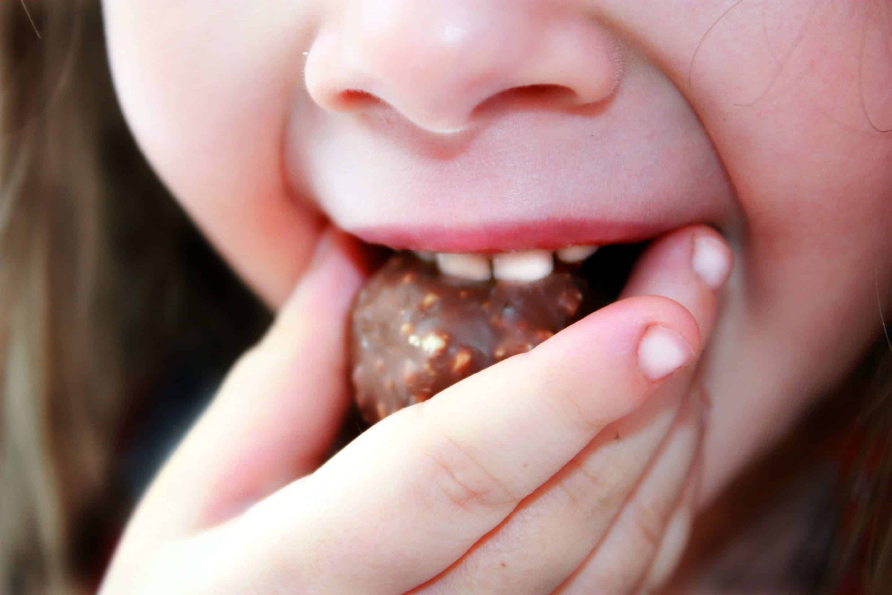 Hand eines kleinen Mädchens schiebt ein Stück Schokolade in den Mund.