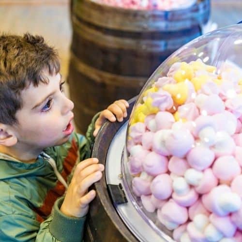 Kleiner Junge steht staunend vor einer großen Schüssel süßer Bonbons.