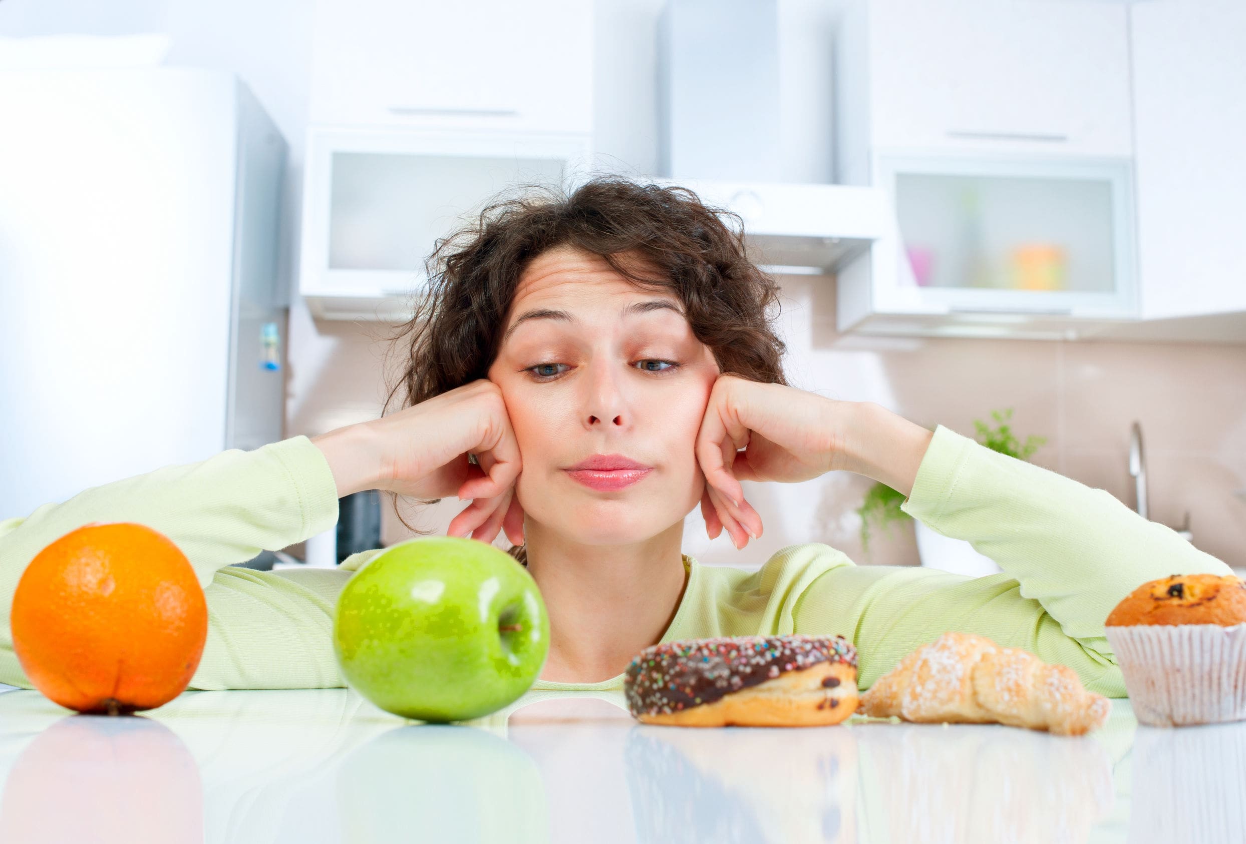 Junge Frau kann sich schwer zwischen Obst und Backwaren entscheiden.